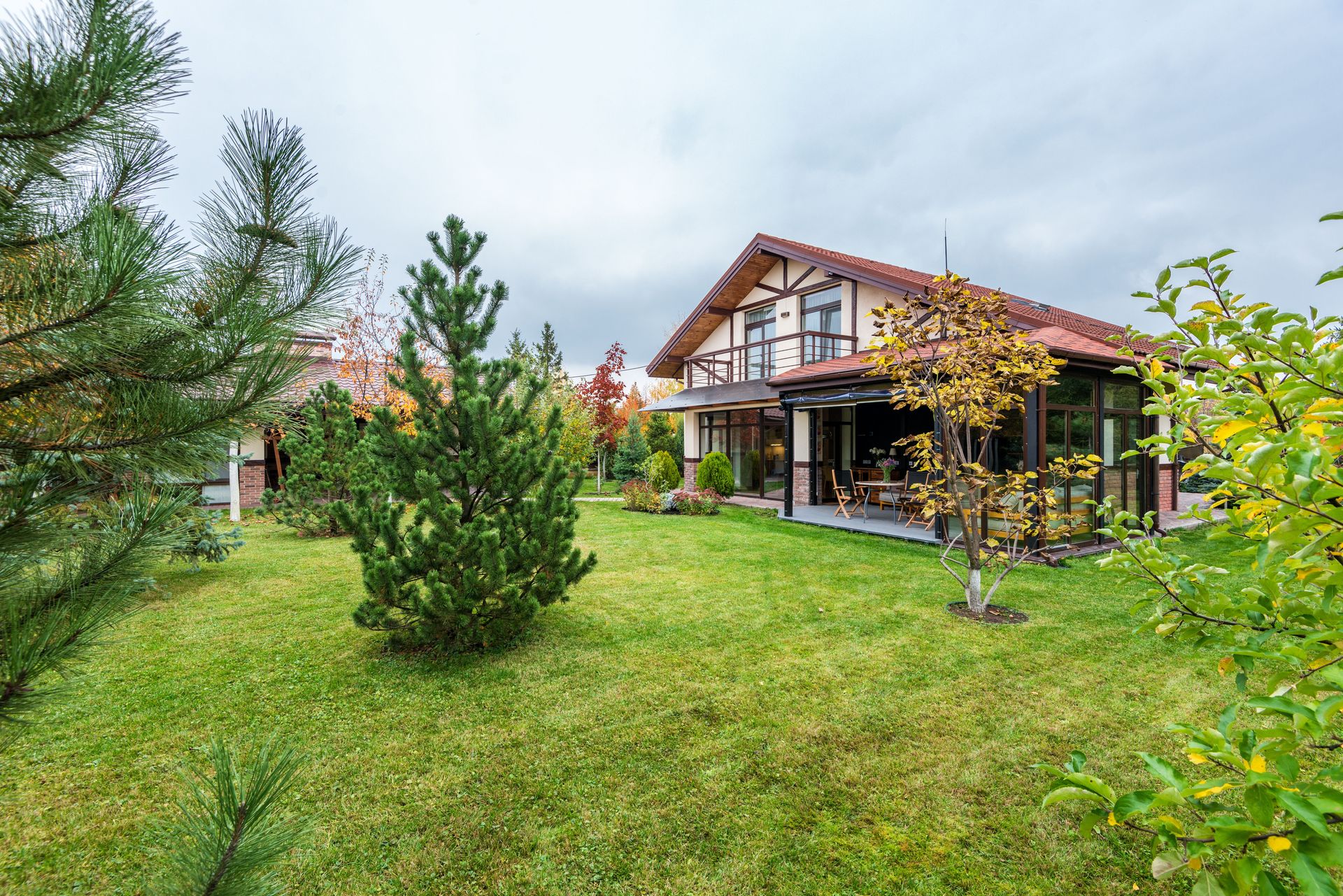 Big private two storey house with terrace surrounded by trees growing on lawn in backyard